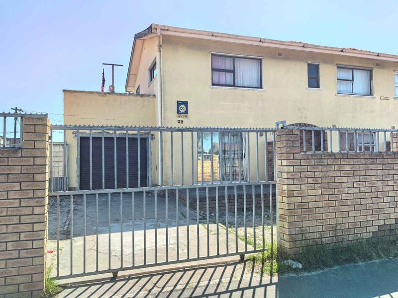 Front exterior view of a townhouse featuring a brick boundary wall, metal security gate, and a single garage.