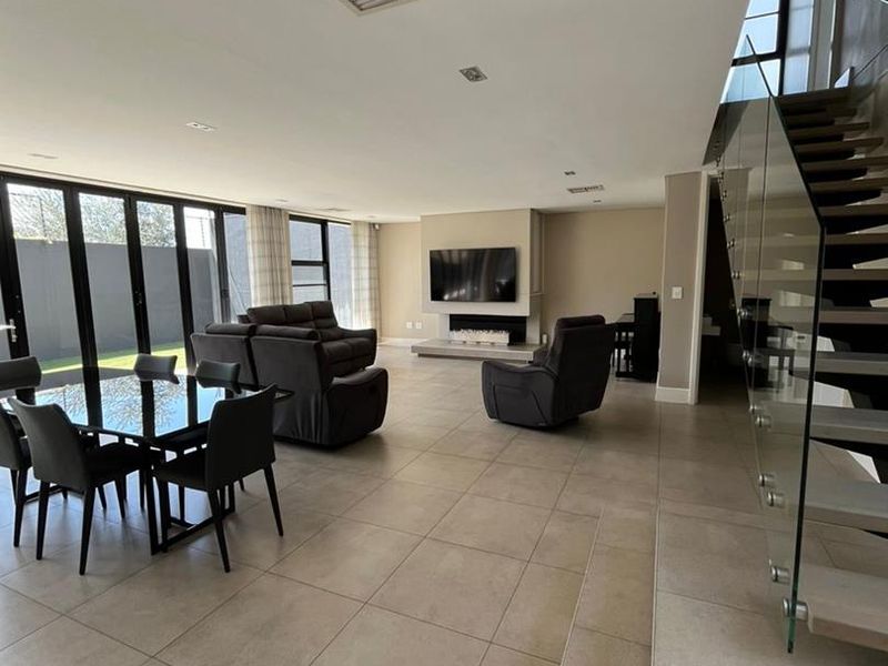 Spacious open-plan living area featuring large format floor tiles, a modern built-in fireplace, and a striking glass balustrade staircase with direct garden access.