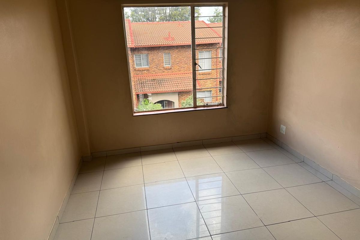 An empty bedroom featuring neutral tiled flooring, a large window with security bars, and a curtain rail, offering a blank canvas for personalization.