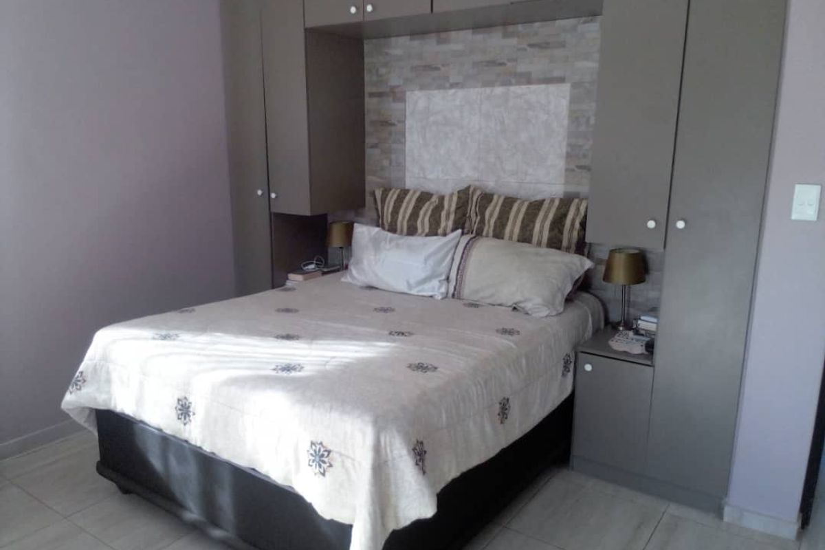 A well-maintained bedroom featuring built-in cupboards with overhead storage and a decorative stone-look feature wall behind the bed area.