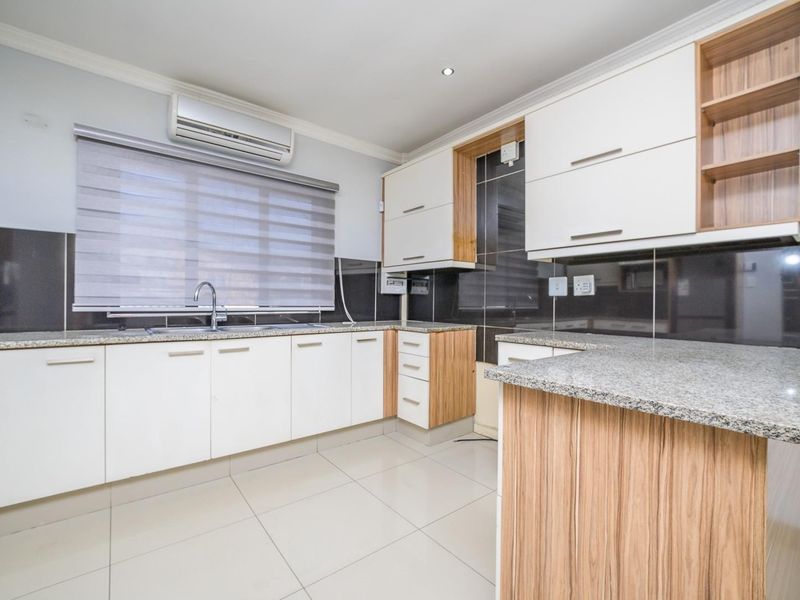 Modern kitchen featuring granite countertops, ample built-in cabinetry, tiled splashbacks, and a split-system air conditioner in a clean, well-maintained space.
