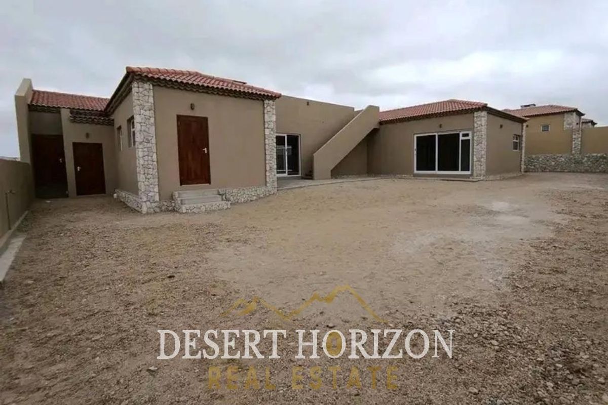 Rear view of a single-story house featuring stone-clad corners, terracotta roof tiles, and an unlandscaped yard area.