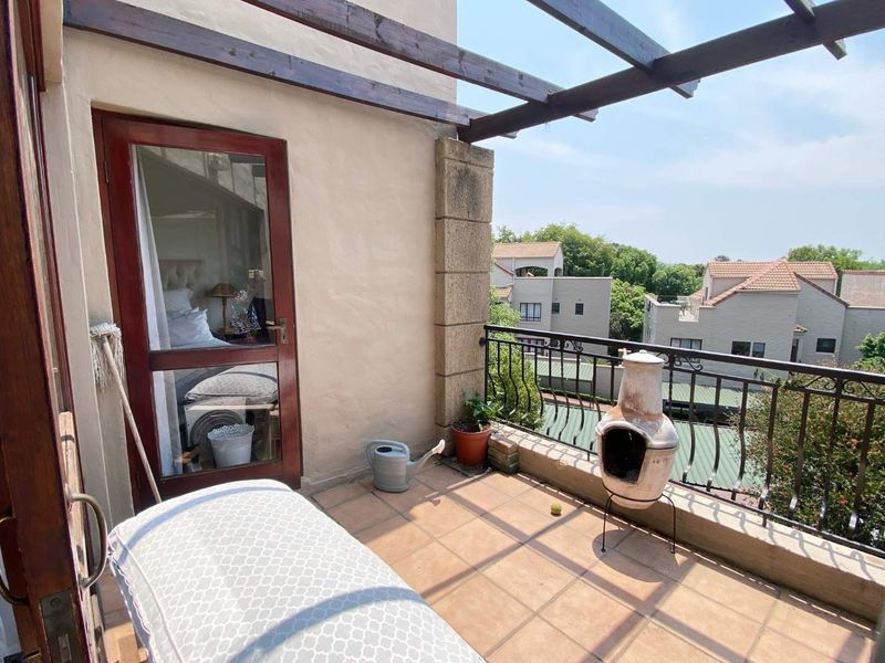 A private balcony featuring a timber pergola, wrought iron balustrade, and tiled flooring, offering an outdoor space accessible via a glass door.