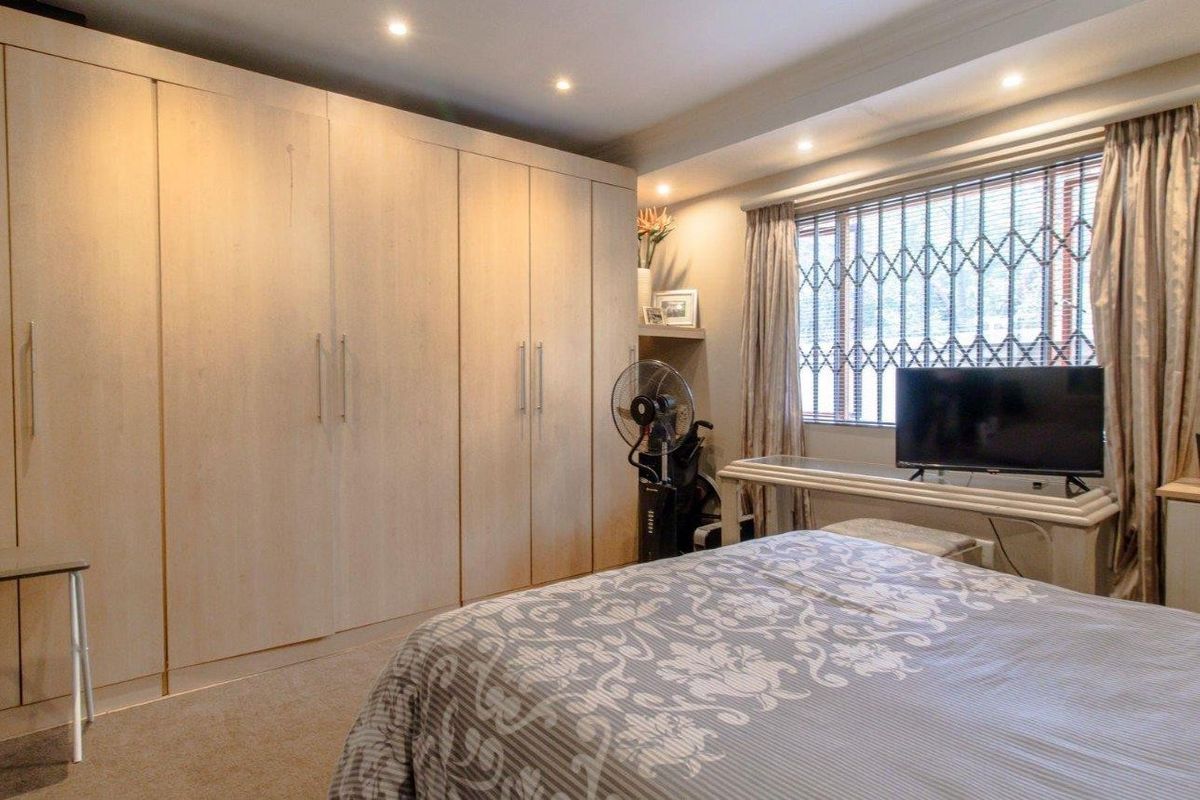 A well-maintained bedroom featuring extensive built-in floor-to-ceiling cabinetry, recessed ceiling lighting, and a window fitted with security bars.