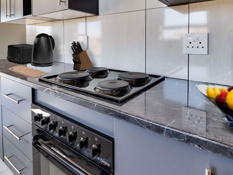 Modern kitchen featuring a sleek electric hob, built-in oven, marble-effect countertops, and contemporary grey cabinetry with a clean tiled backsplash.
