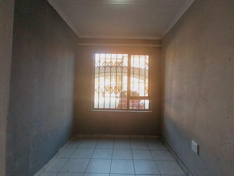 An empty, unfinished bedroom featuring tiled flooring and a window with security bars, offering a blank canvas for renovation.