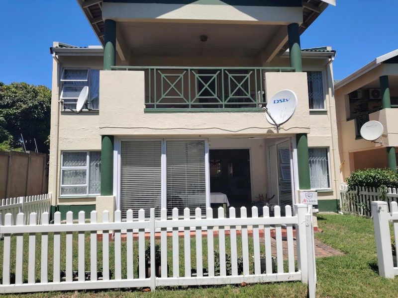 Rear view of a two-story apartment unit featuring a ground-floor patio with sliding doors, an upper-level balcony, and a private fenced garden area.