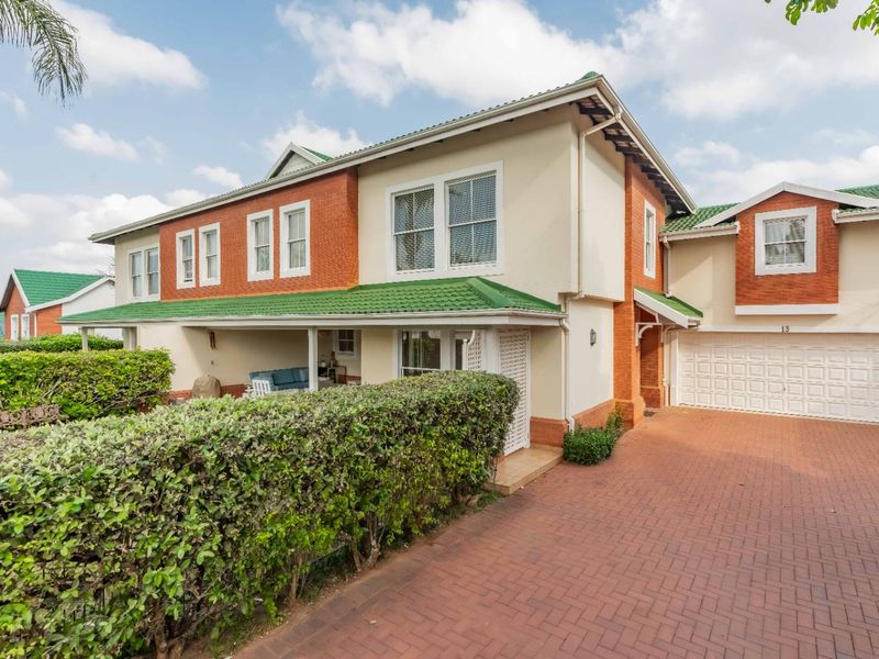 Front elevation of a two-story townhouse featuring a brick driveway, integrated garage, and a covered patio area with established garden hedging.