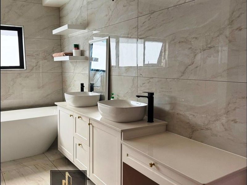 Modern bathroom featuring a double vanity with vessel sinks, black fixtures, a freestanding bathtub, and elegant marble-look wall tiling.