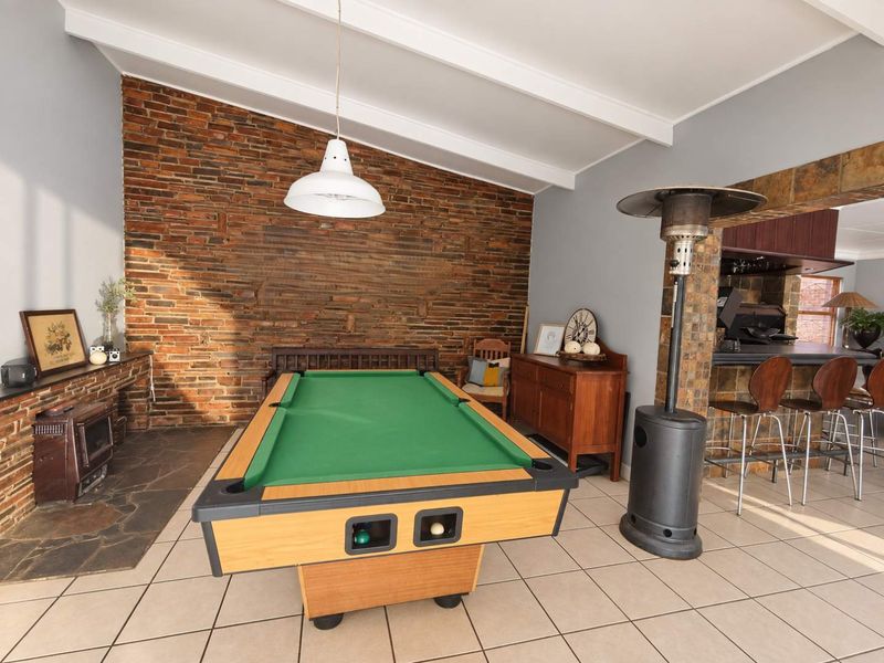 Spacious living area featuring a striking exposed brick wall, vaulted ceilings with exposed beams, tiled flooring, and a built-in fireplace with a stone hearth.