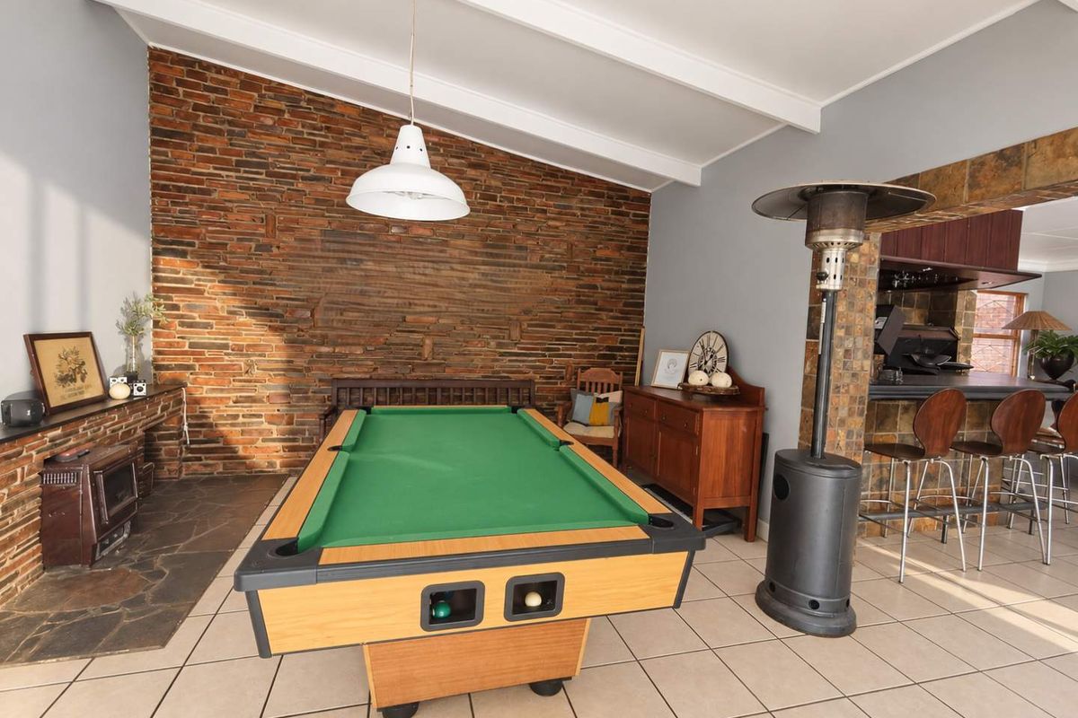 Spacious living area featuring a striking exposed brick wall, vaulted ceilings with exposed beams, tiled flooring, and a built-in fireplace with a stone hearth.