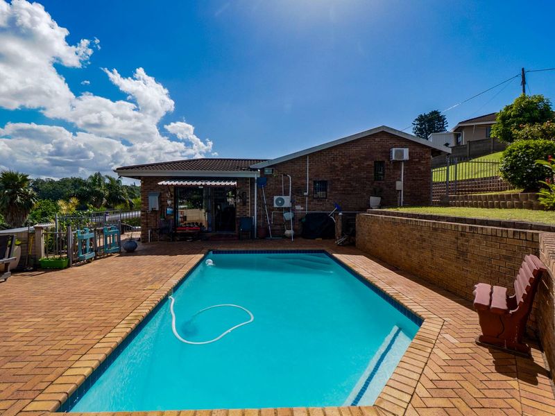 Outdoor pool area featuring a swimming pool, brick paved surround, and a retaining wall, set against the rear brick facade of the house.