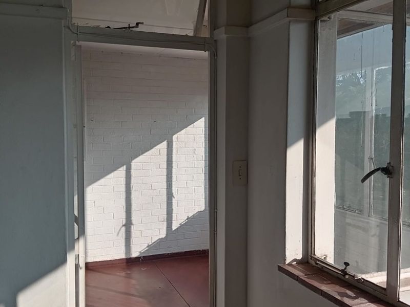 A vacant hallway featuring steel-framed windows, painted brick walls, and tiled flooring, showing signs of wear and requiring cosmetic updates.