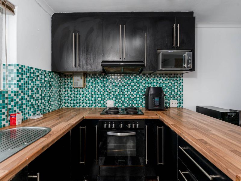 Compact kitchen featuring black cabinetry, wood-look countertops, and a vibrant green mosaic tile backsplash, equipped with a built-in oven and hob.