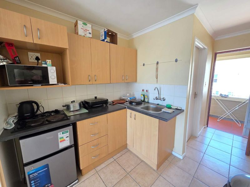 A compact kitchen featuring laminate cabinetry, a stainless steel sink, electric hob, and ceramic tile flooring, with direct access to an outdoor balcony area.