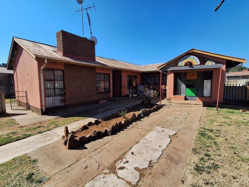 Front view of a single-story brick house featuring a concrete driveway, security bars on windows, and a metal roof.