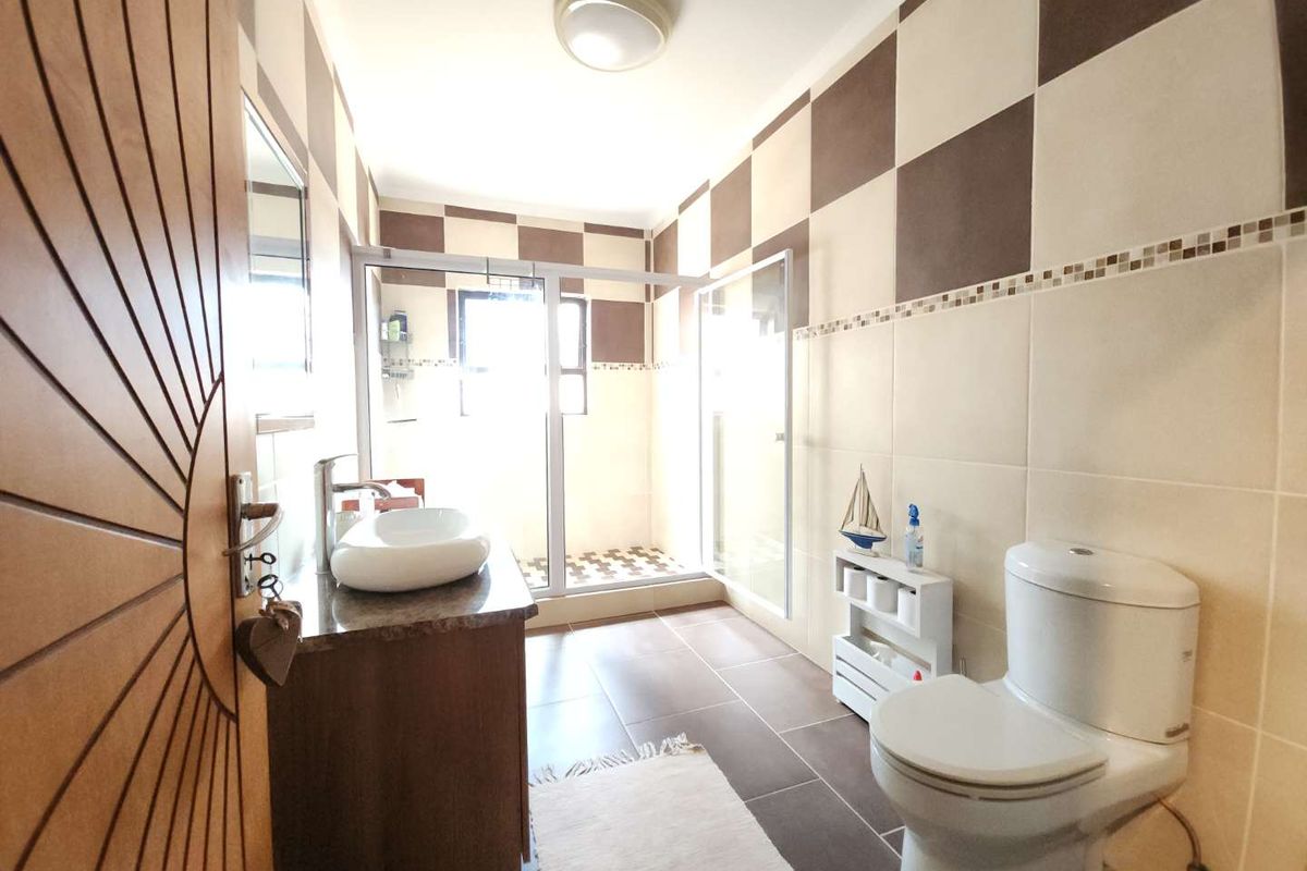 A functional bathroom featuring a vanity with a vessel sink, a glass-enclosed shower, and a standard toilet with checkered wall tiling.