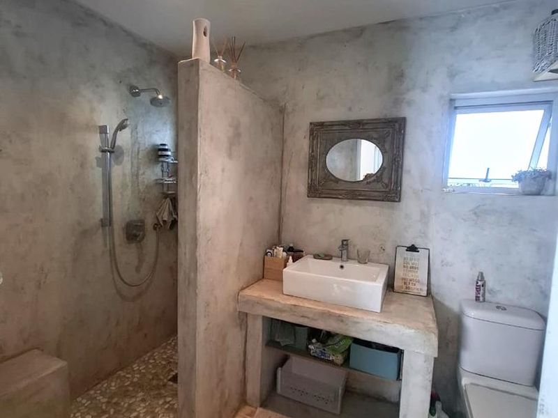Modern bathroom featuring a walk-in shower with pebble flooring, a custom concrete vanity with a vessel sink, and a neutral cement-style finish.