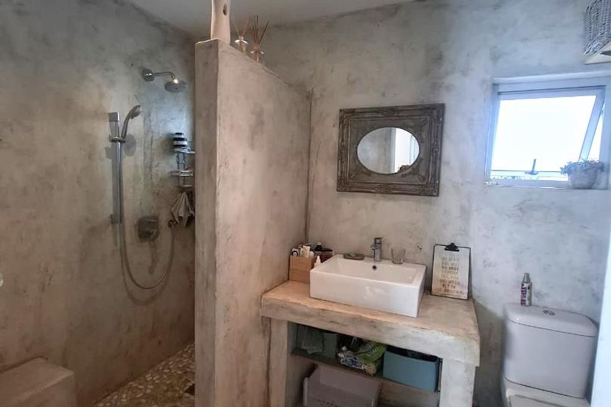 Modern bathroom featuring a walk-in shower with pebble flooring, a custom concrete vanity with a vessel sink, and a neutral cement-style finish.