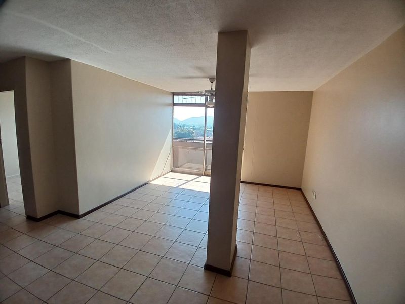An empty, open-plan living area featuring ceramic tile flooring, a central structural column, and a sliding glass door leading to a balcony with views.