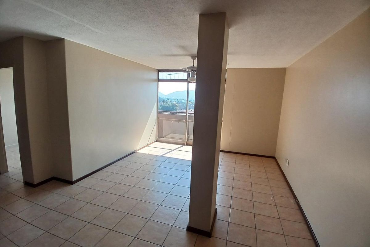 An empty, open-plan living area featuring ceramic tile flooring, a central structural column, and a sliding glass door leading to a balcony with views.