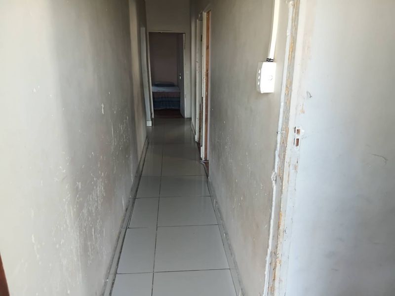 A narrow hallway featuring tiled flooring and multiple doorways, currently showing significant wear and tear on the wall surfaces and door frames.