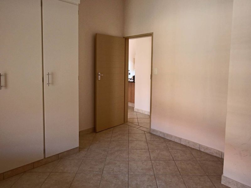 An empty bedroom featuring tiled flooring and built-in white cupboards, with a doorway leading to an adjacent room.