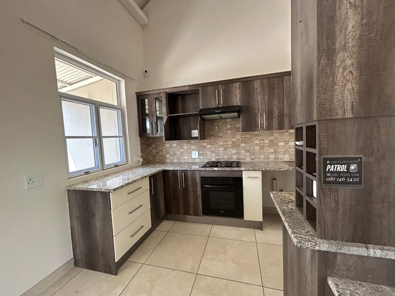 A modern kitchen featuring granite countertops, built-in oven, gas hob, extractor fan, and ample cabinetry, set under a high vaulted ceiling.
