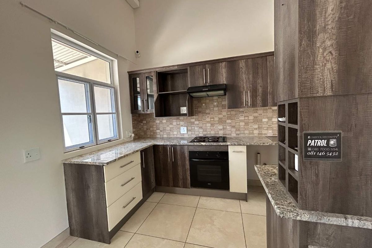 A modern kitchen featuring granite countertops, built-in oven, gas hob, extractor fan, and ample cabinetry, set under a high vaulted ceiling.