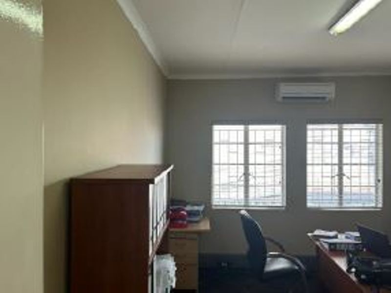 A functional office space featuring dual windows with security bars, wall-mounted air conditioning, and overhead fluorescent lighting.