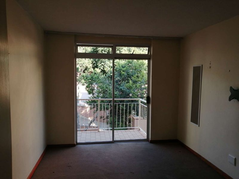 An empty living room featuring carpet flooring, a wall-mounted heater, and a sliding glass door providing access to a private balcony.