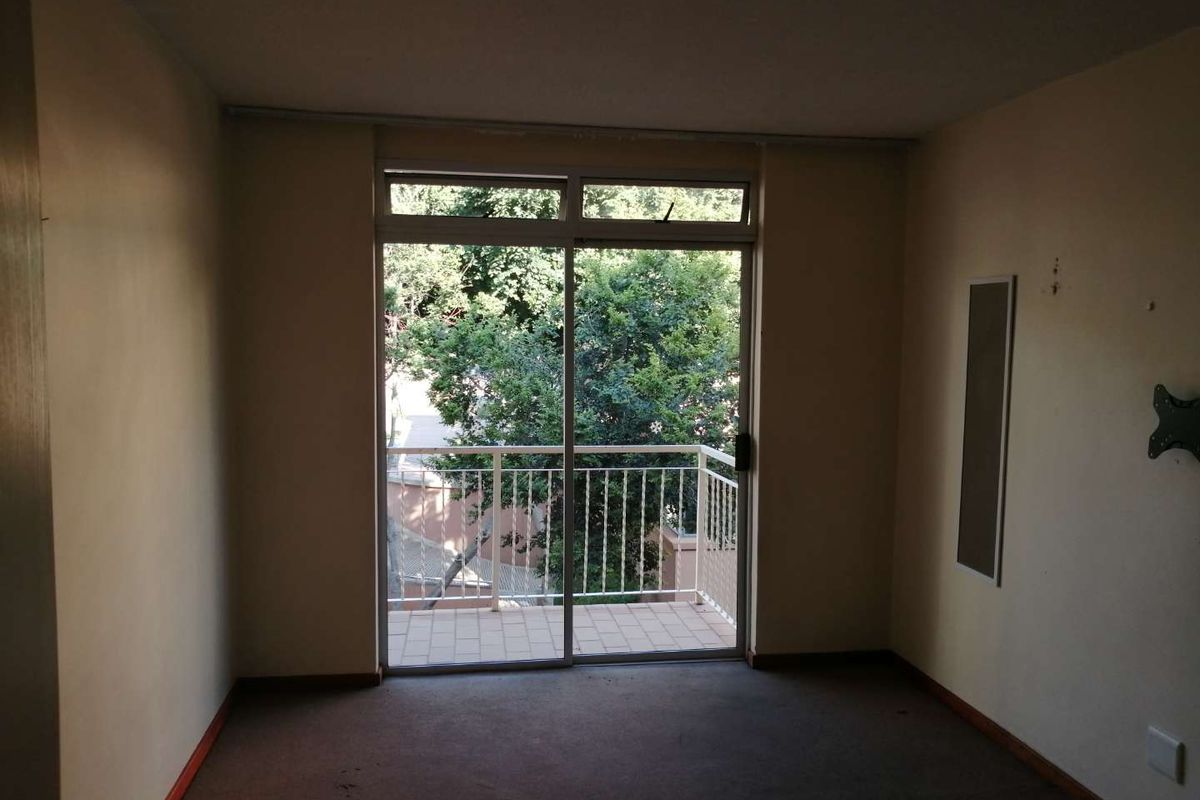 An empty living room featuring carpet flooring, a wall-mounted heater, and a sliding glass door providing access to a private balcony.