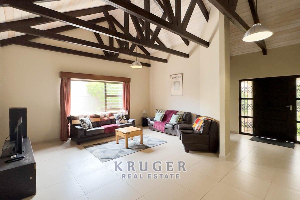 Spacious living room featuring high vaulted ceilings with exposed timber trusses, tiled flooring, and a secure entrance door with security gate.