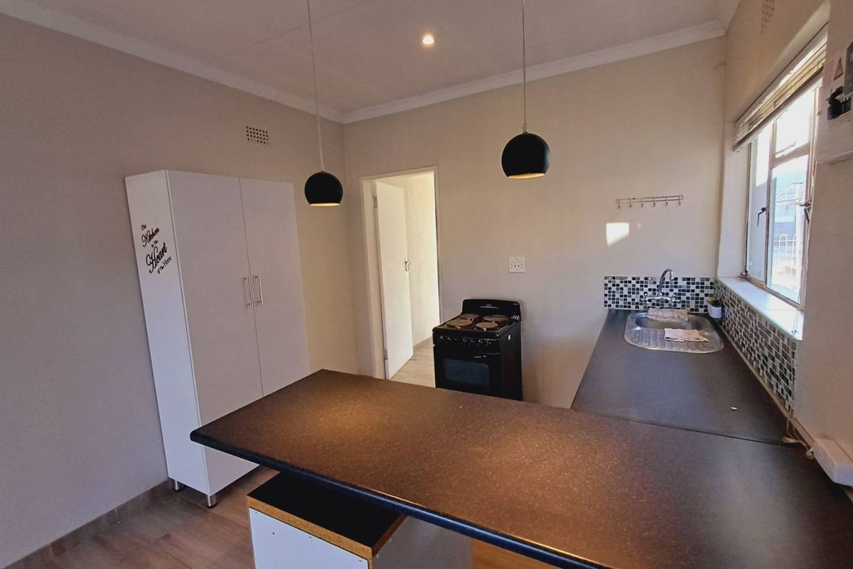 A functional kitchen featuring laminate countertops, a mosaic tile backsplash, stainless steel sink, and a freestanding stove with modern pendant lighting.