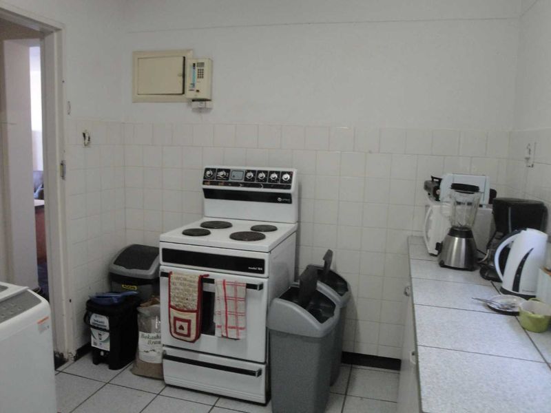 A functional kitchen area featuring a freestanding electric stove, tiled splashbacks, and tiled flooring, offering a dated but practical layout.