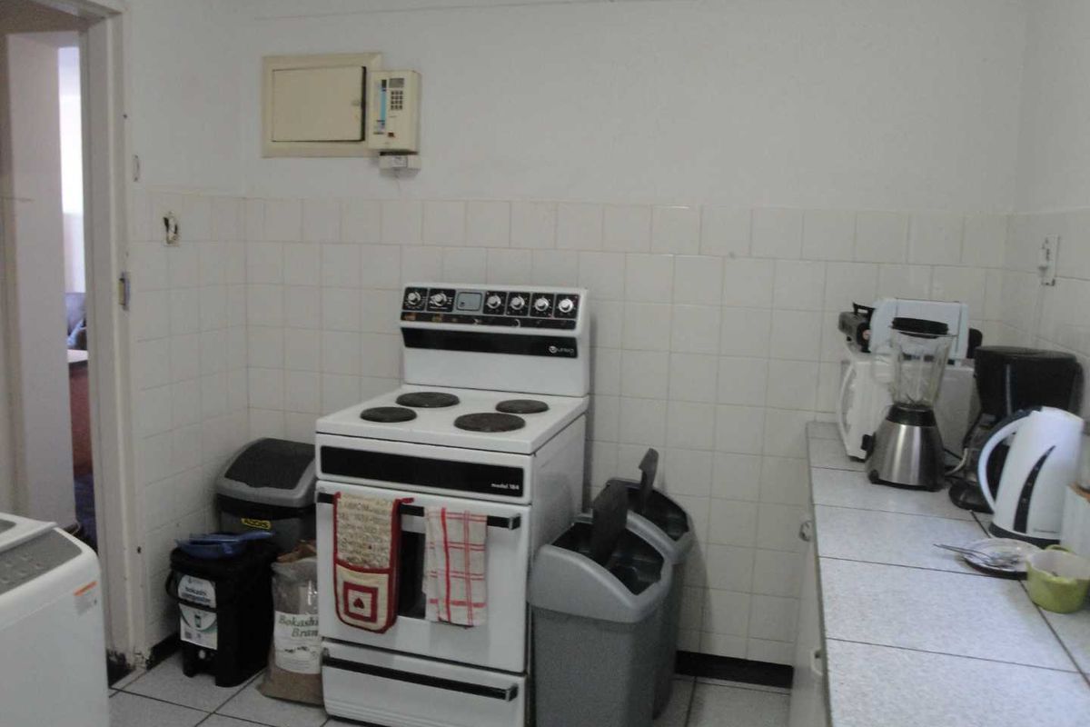 A functional kitchen area featuring a freestanding electric stove, tiled splashbacks, and tiled flooring, offering a dated but practical layout.