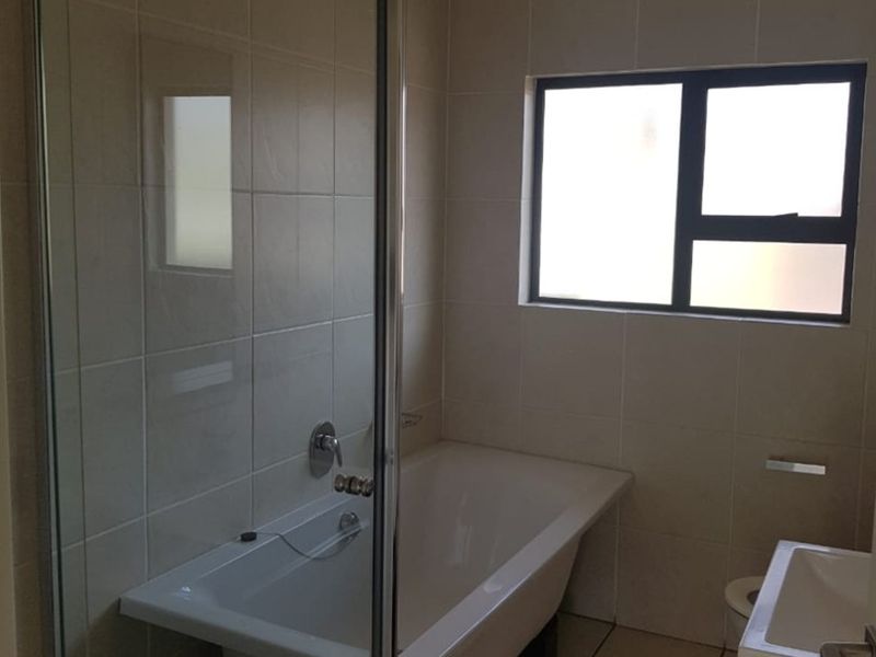 A functional bathroom featuring a shower enclosure, bathtub, vanity basin, and neutral tiled finishes with a frosted window for privacy.