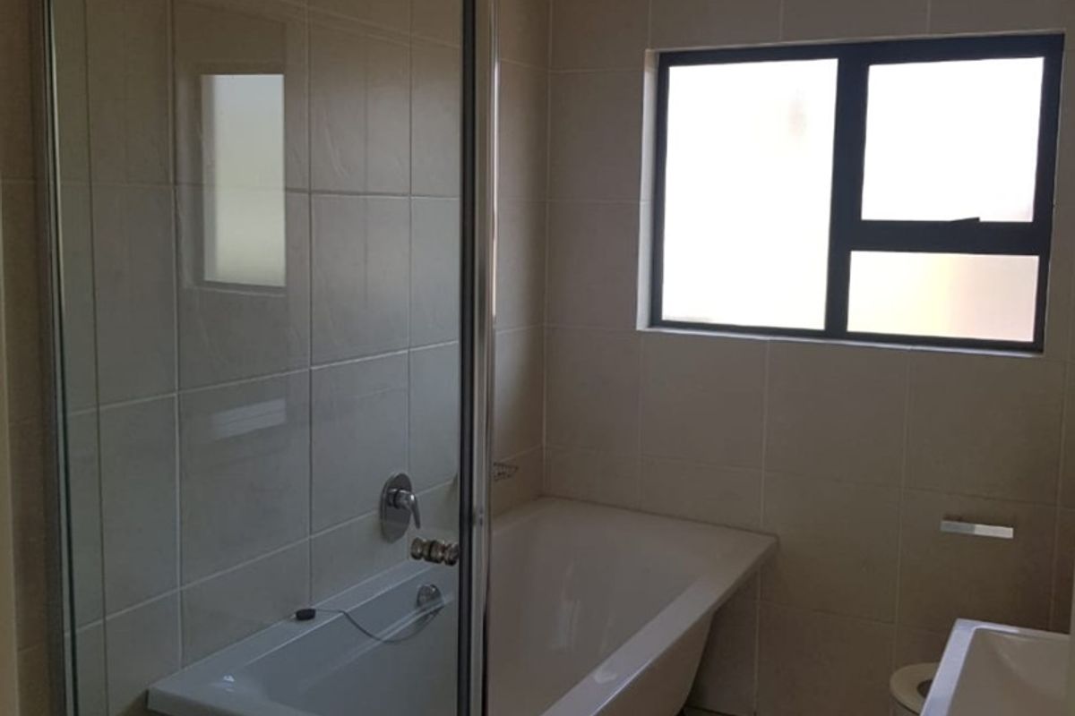 A functional bathroom featuring a shower enclosure, bathtub, vanity basin, and neutral tiled finishes with a frosted window for privacy.