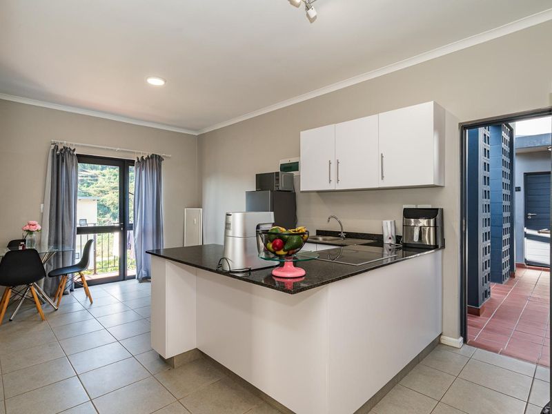Open-plan kitchen and dining area featuring granite countertops, white cabinetry, and direct access to a balcony through a glass sliding door.