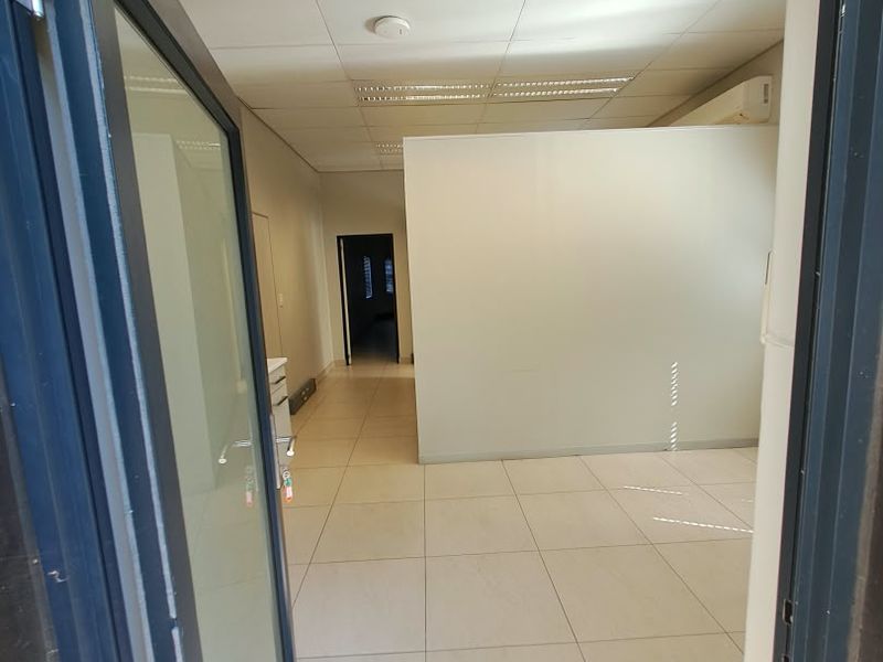 An empty office space featuring tiled flooring, a suspended ceiling with recessed lighting, and a partition wall, providing a clean and functional workspace.