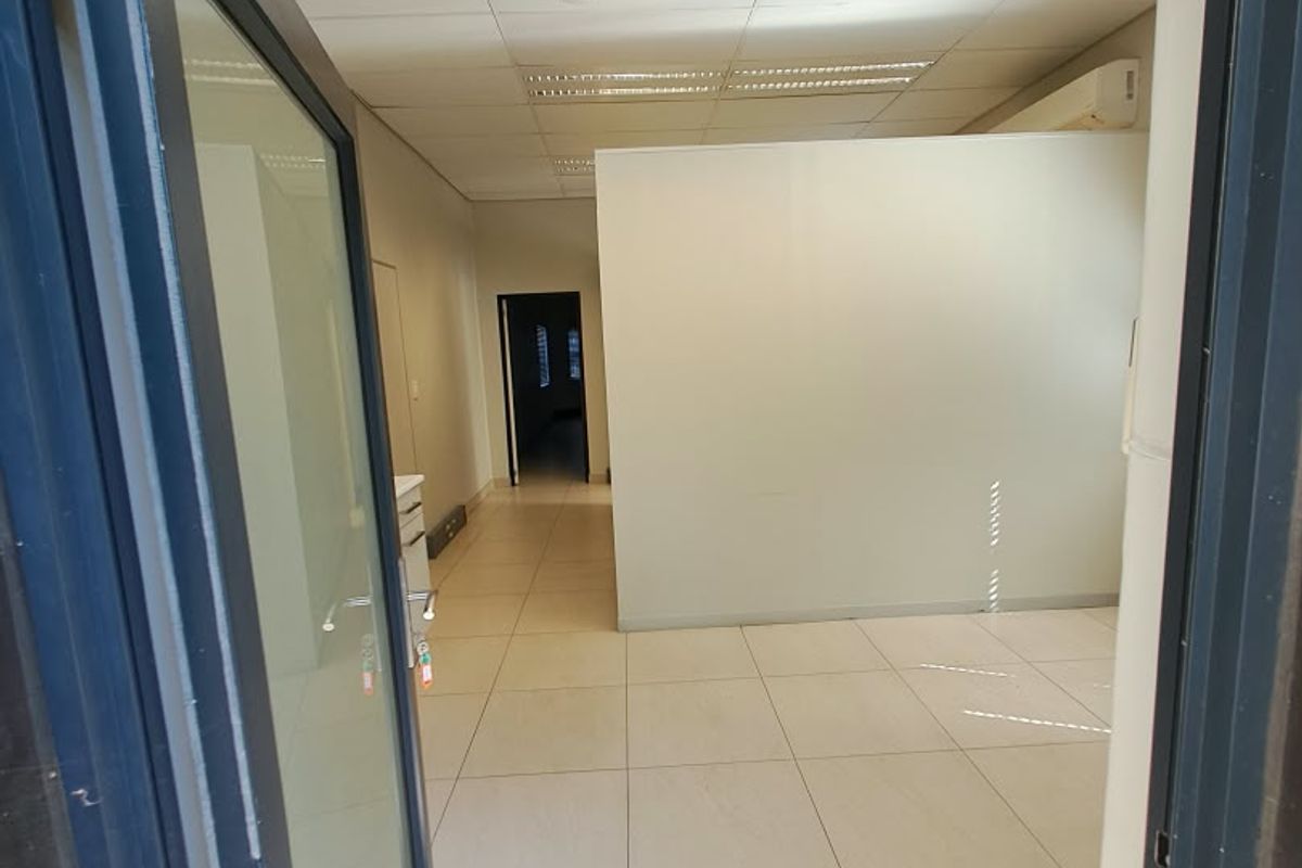 An empty office space featuring tiled flooring, a suspended ceiling with recessed lighting, and a partition wall, providing a clean and functional workspace.