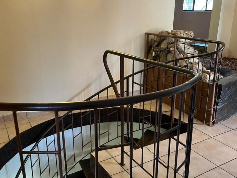 A hallway area featuring a spiral staircase with a metal balustrade and tiled flooring, leading to a lower level.