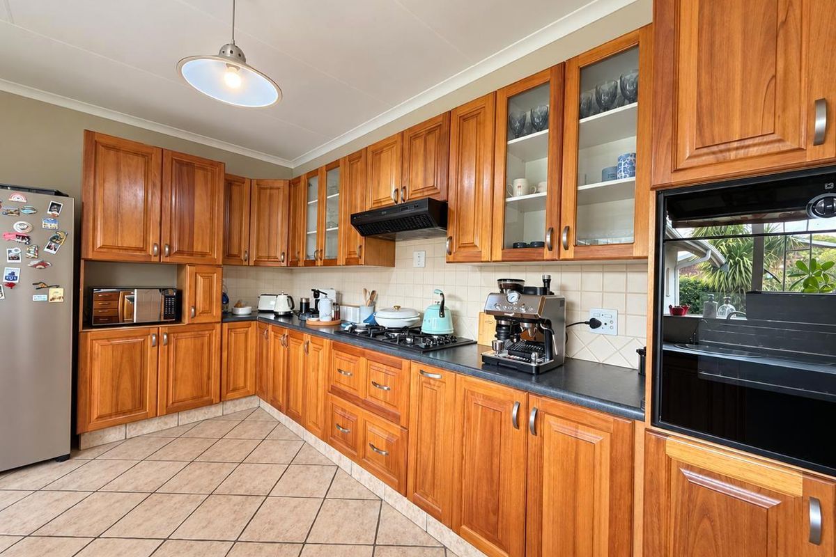 A functional kitchen featuring warm-toned wooden cabinetry, dark laminate countertops, a built-in oven, gas hob, and tiled flooring throughout.