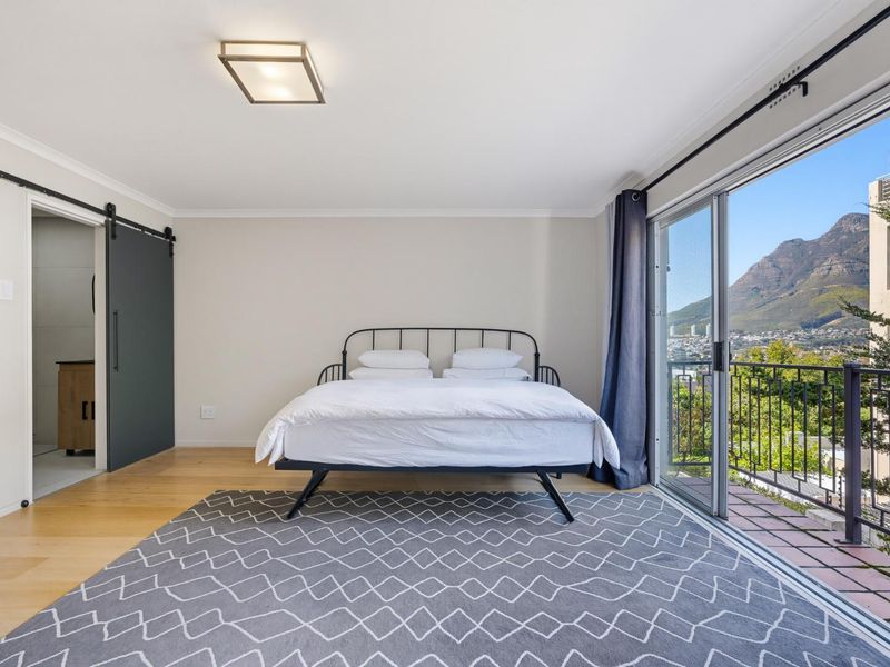 Spacious bedroom featuring hardwood flooring, a modern sliding barn door, and large glass sliding doors opening to a balcony with mountain views.