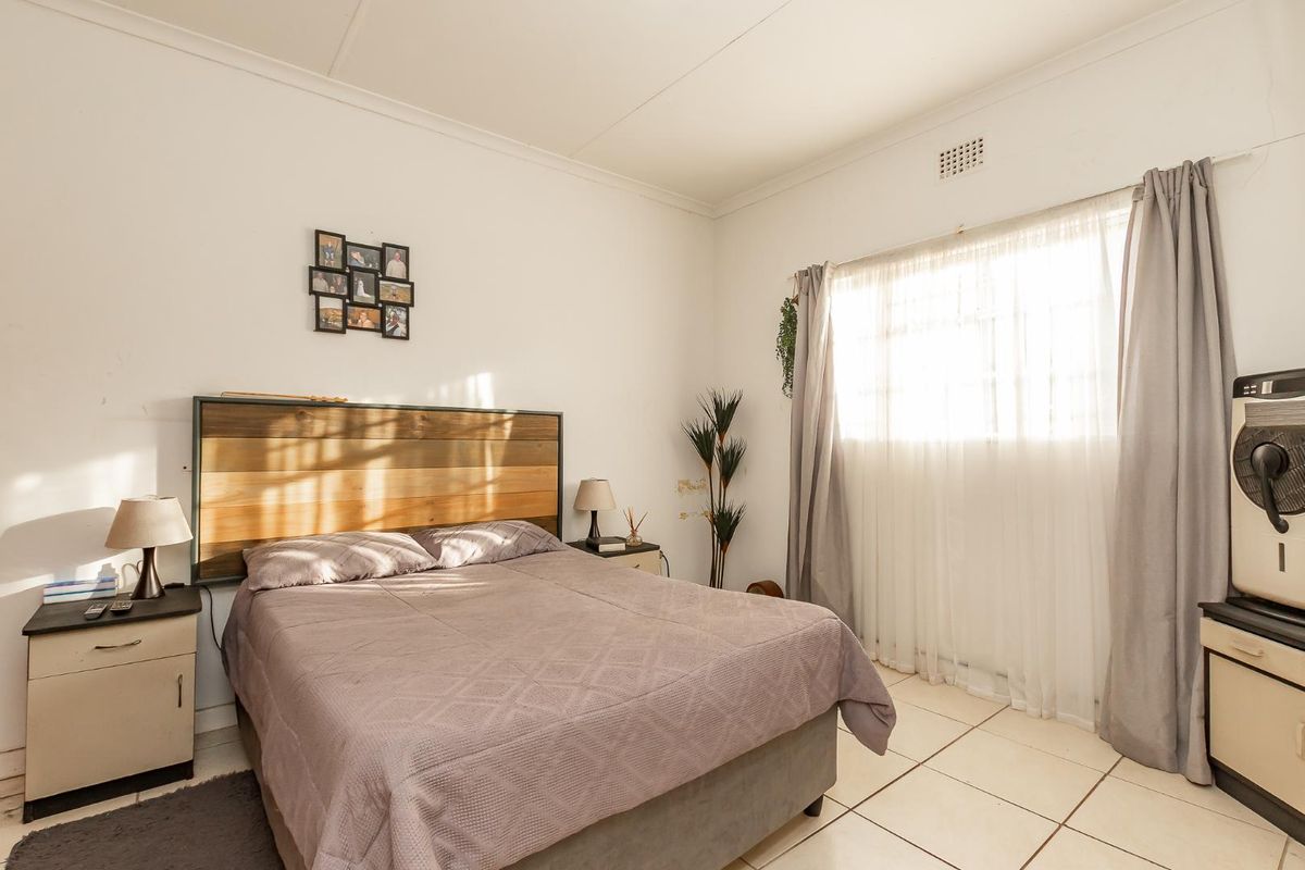 A well-lit bedroom featuring neutral tiled flooring and a large window with curtain treatments.