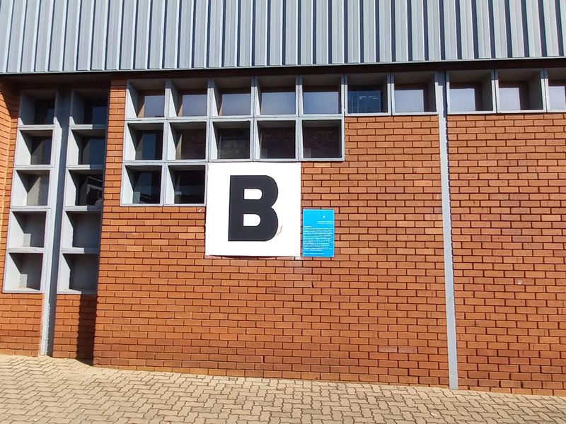 Exterior view of an industrial building facade featuring red brickwork, metal cladding, and a grid of square windows with a unit B identifier.