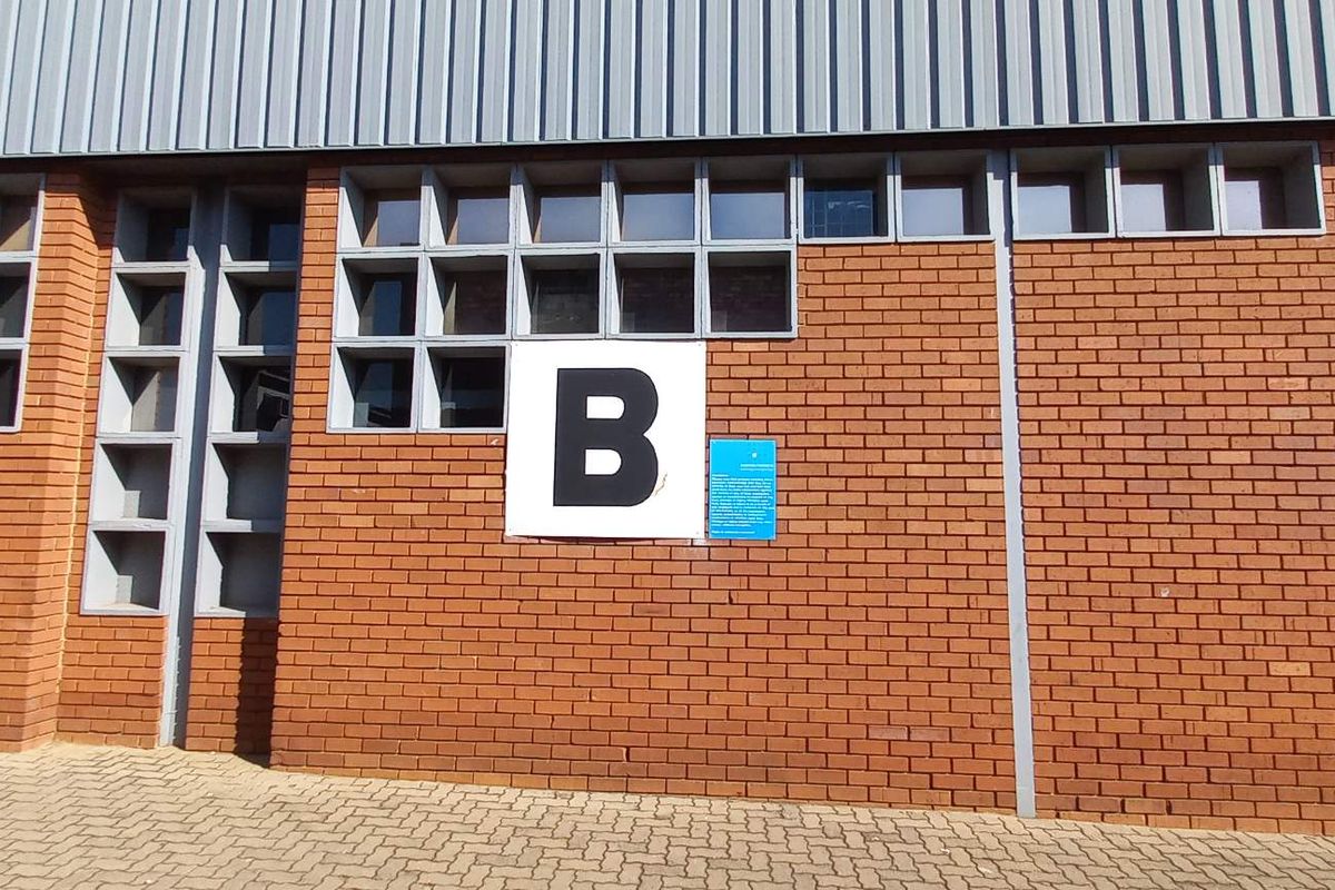 Exterior view of an industrial building facade featuring red brickwork, metal cladding, and a grid of square windows with a unit B identifier.