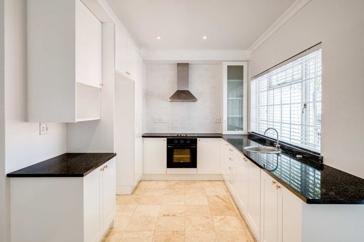 A clean, modern kitchen featuring white cabinetry, dark granite countertops, built-in appliances, and neutral tiled flooring with ample natural light.
