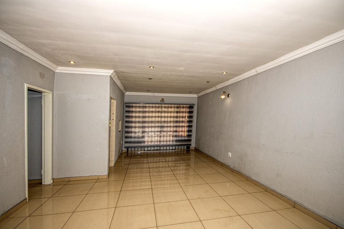 An empty, neutrally painted living room featuring tiled flooring, recessed downlighting, and a security gate over the window.