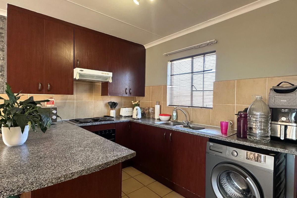 Functional kitchen featuring dark wood cabinetry, granite-look countertops, tiled splashbacks, and integrated appliances including a hob and extractor fan.